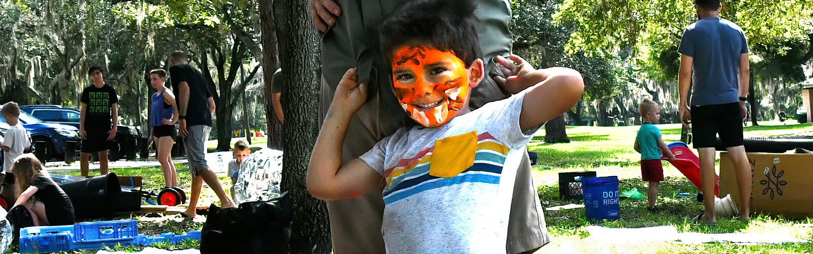 Leaning against his father, Thomas, 4, shyly expresses his joy at his newly-painted tiger face during the Mud Day event.