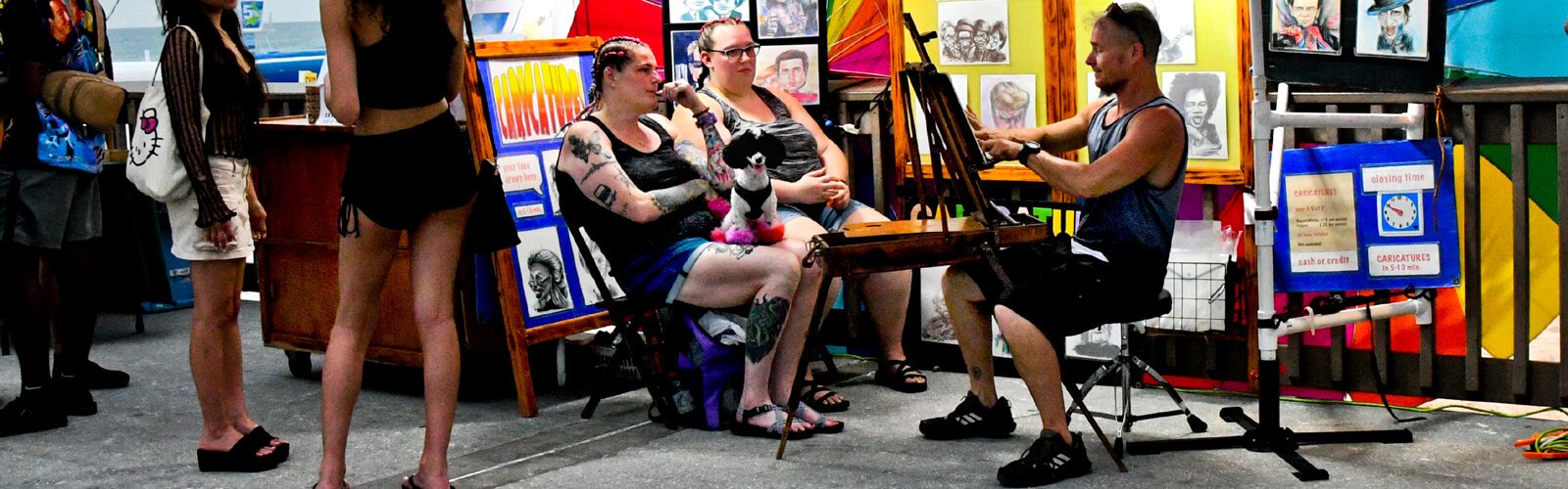  Two visitors with their dog sit for their “Caricature by Gordon” at Pier 60.