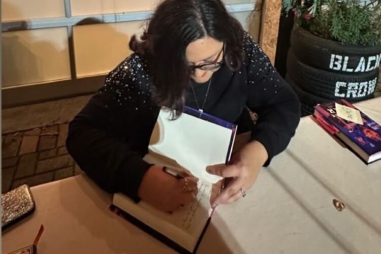 St. Pete poet laureate Gloria Muñoz signs a copy of her debut novel "This is the Year" during a book launch event at Tombolo Books